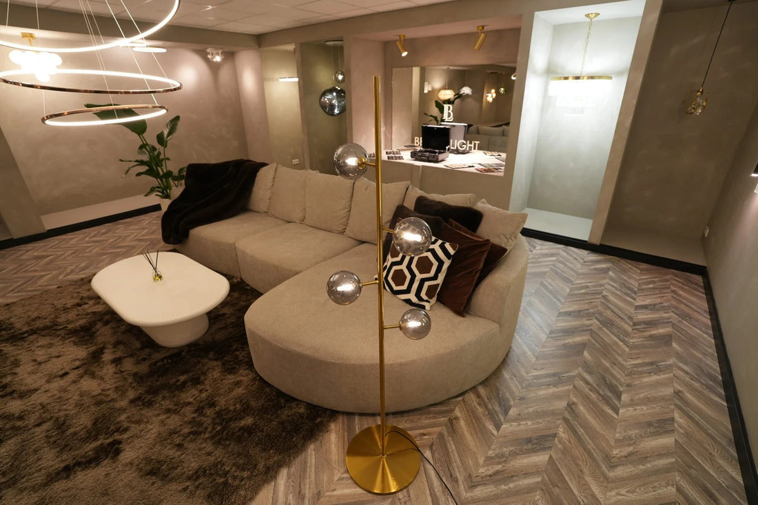 Gouden vloerlamp met glazen bollen naast een ronde bank in de showroom van Best in Light