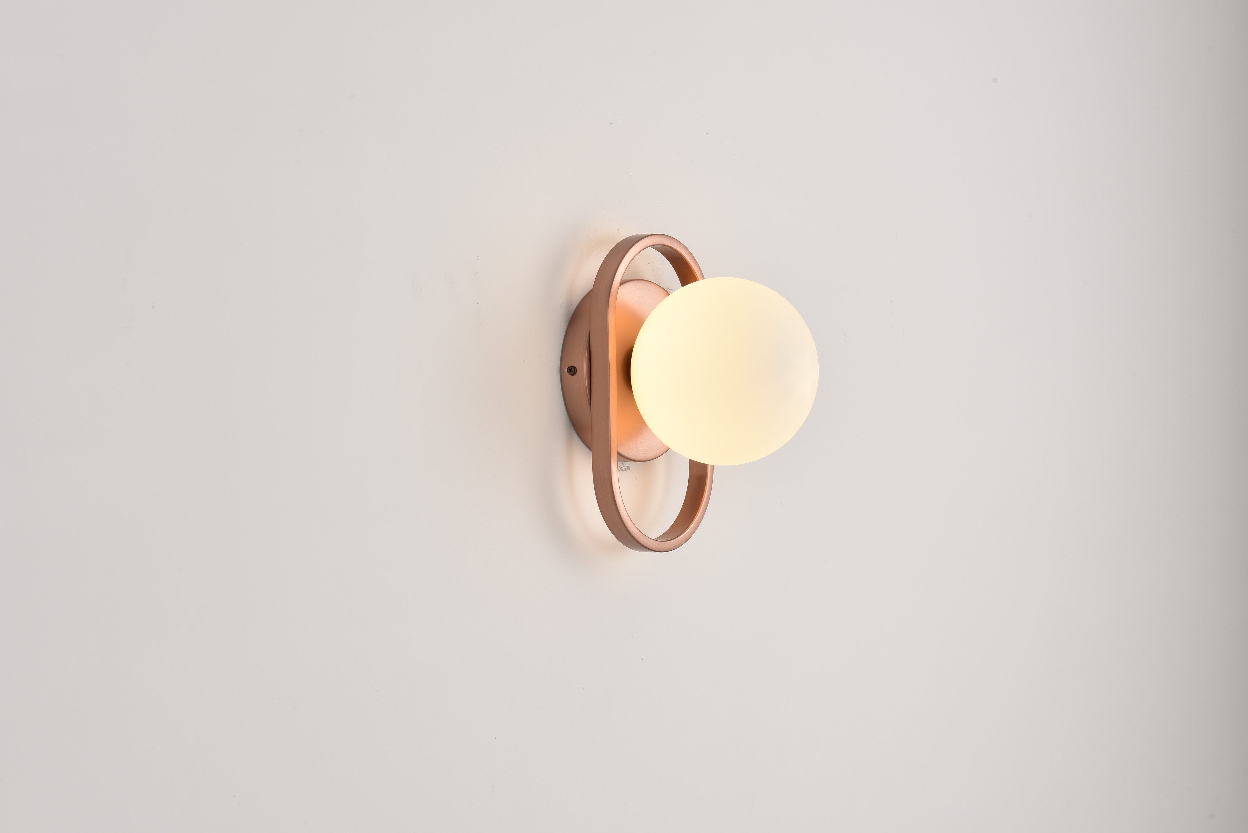 Wandlamp Jessica in brons brandend met zacht licht tegen een lichte wand