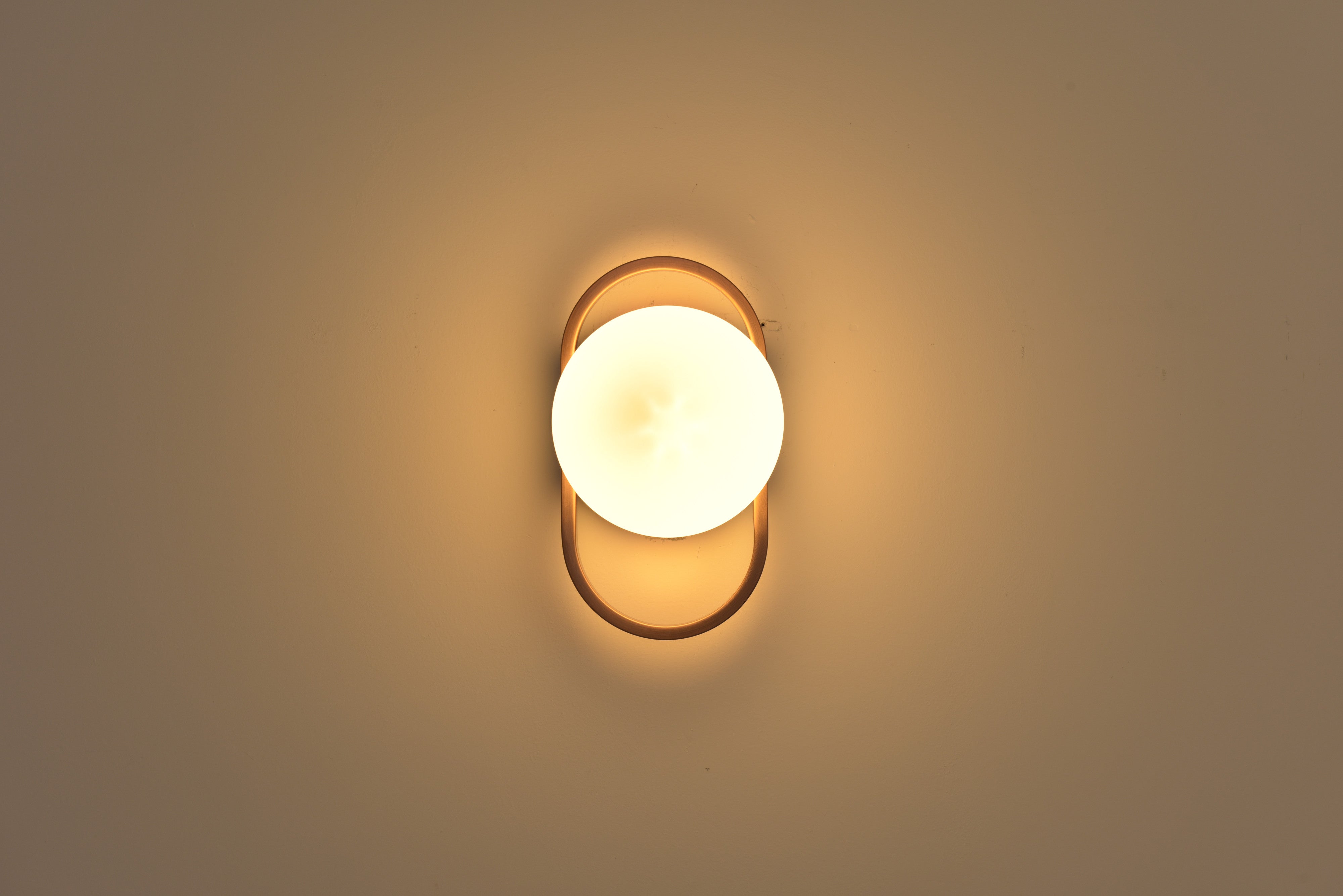 Wandlamp Jessica in brons recht van voren brandend met de bol in de ovale ring