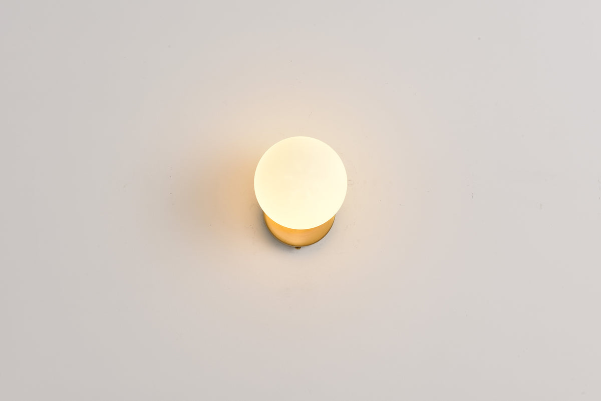 Wandlamp Maria in goud brandend, recht van voren tegen een lichte wand