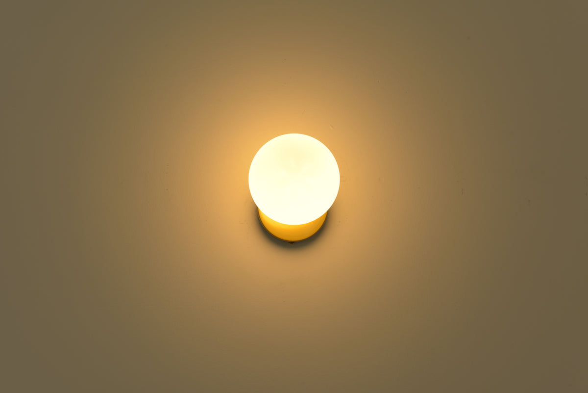 Wandlamp Maria in goud brandend in een donkere ruimte met warme lichtkring