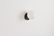 Wandlamp Maria in zwart met opaalwitte bol op een witte wand