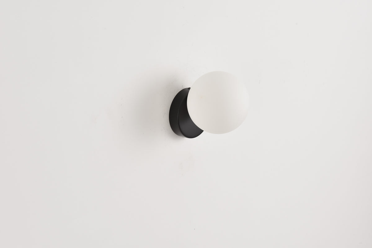 Wandlamp Maria in zwart met opaalwitte bol op een witte wand
