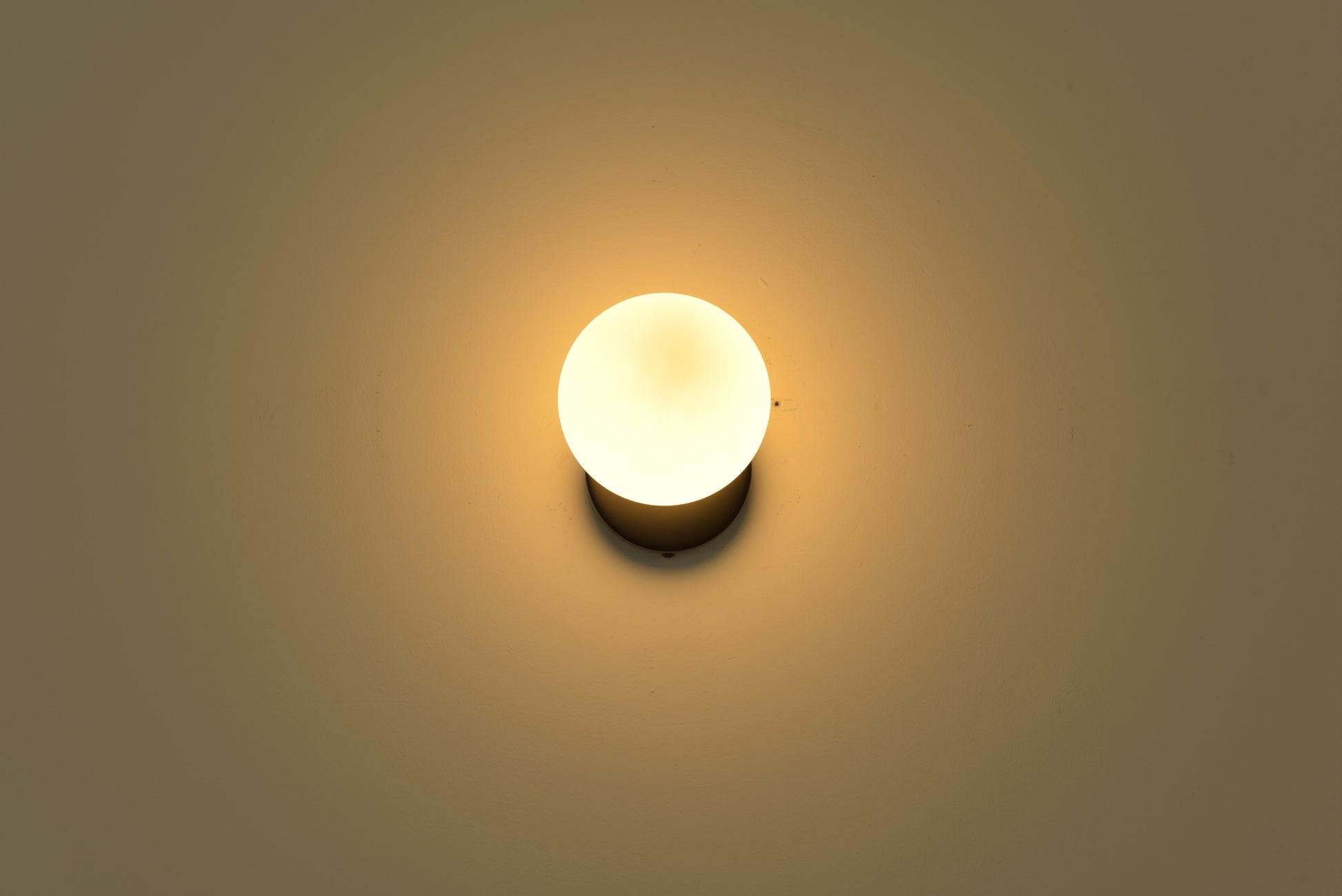 Wandlamp Maria in zwart brandend in een donkere ruimte met warme gloed