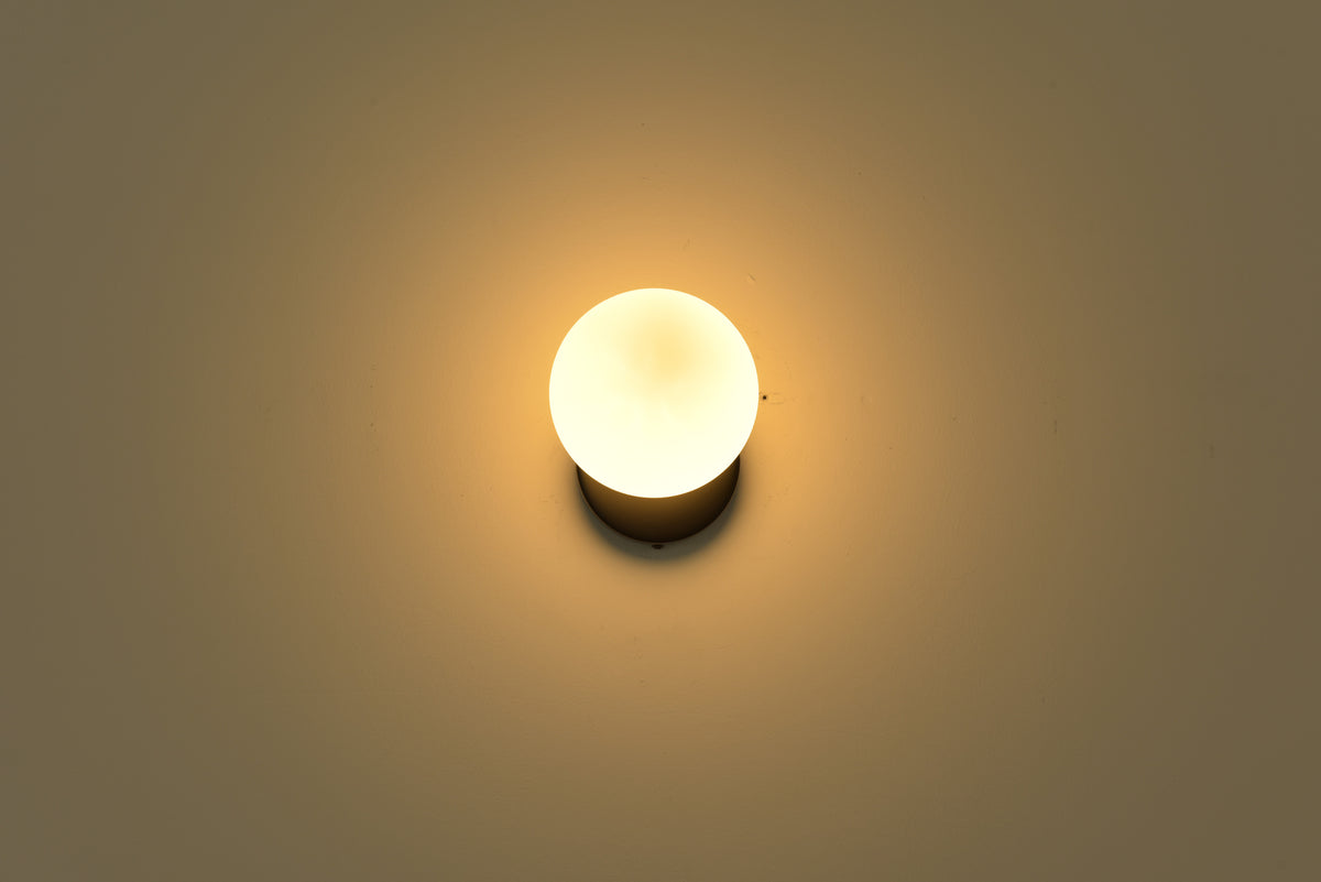 Wandlamp Maria in zwart brandend in een donkere ruimte met warme gloed