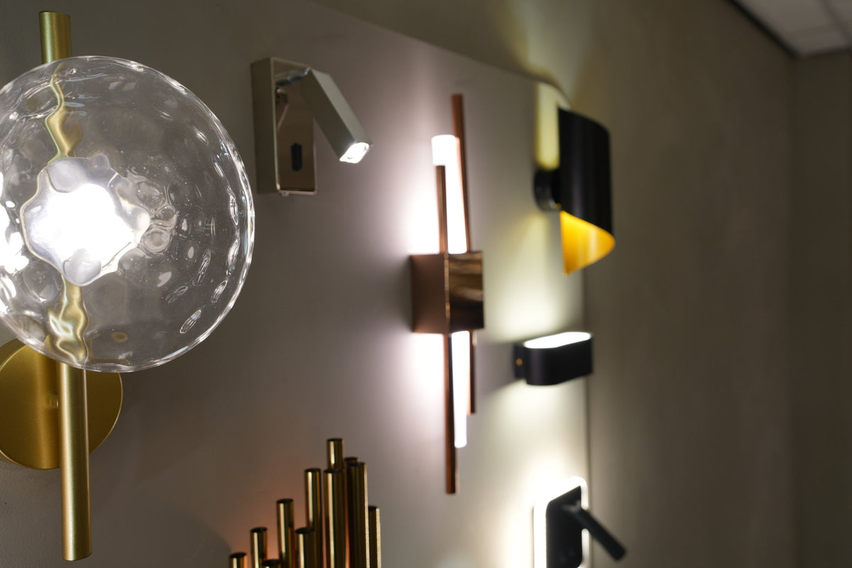 Wandlampen naast elkaar op de muur, van glas tot messing