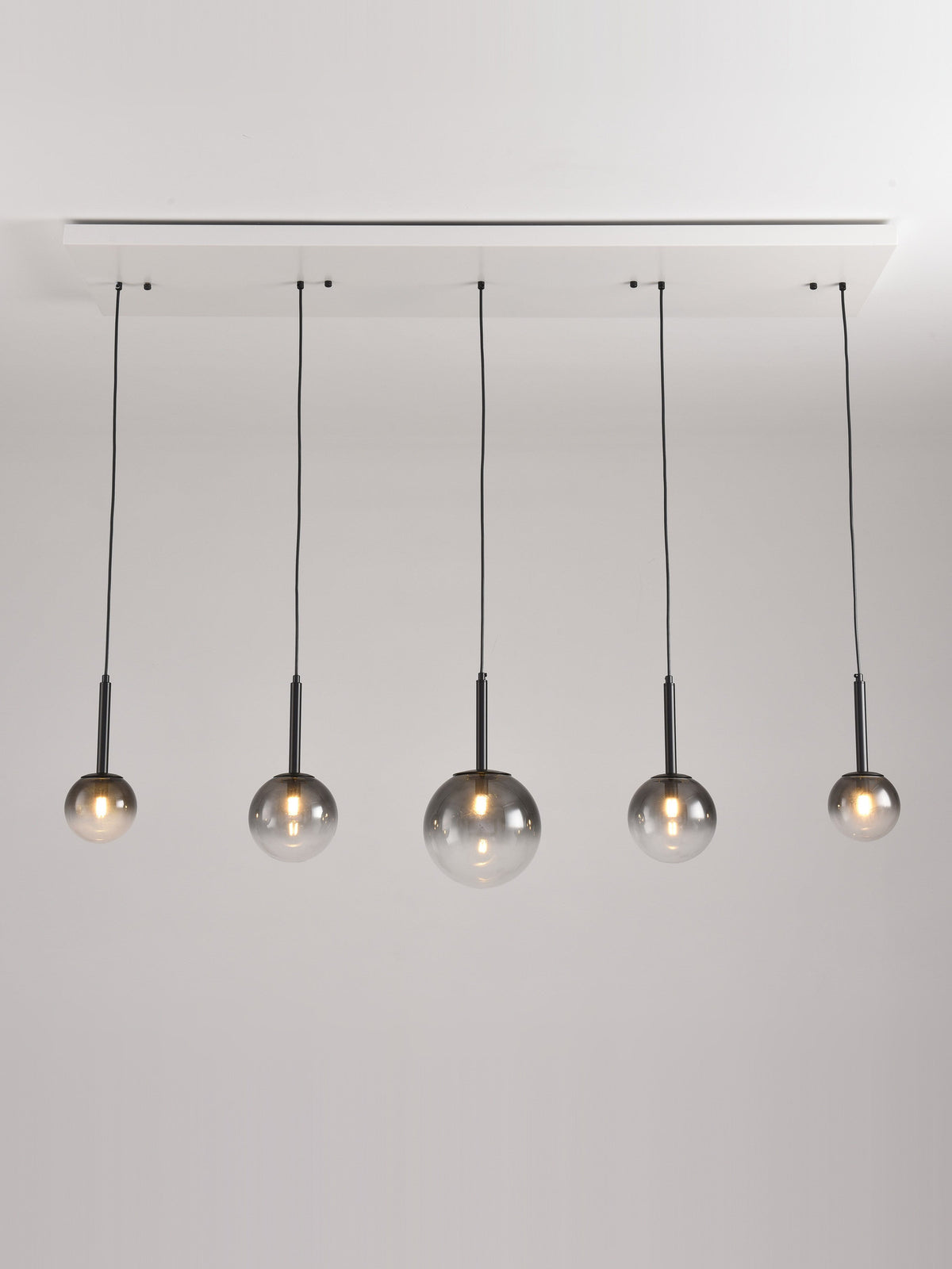 Hanglamp Stellar met vijf rookglazen bollen aan een langwerpige plafondplaat
