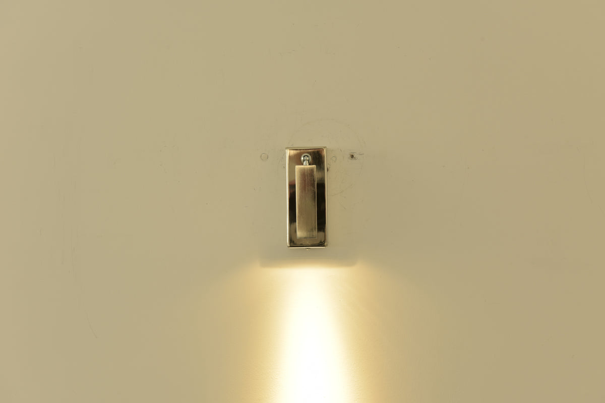 Wandlamp Vero in nikkel ingeklapt en brandend met een lichtbundel omlaag