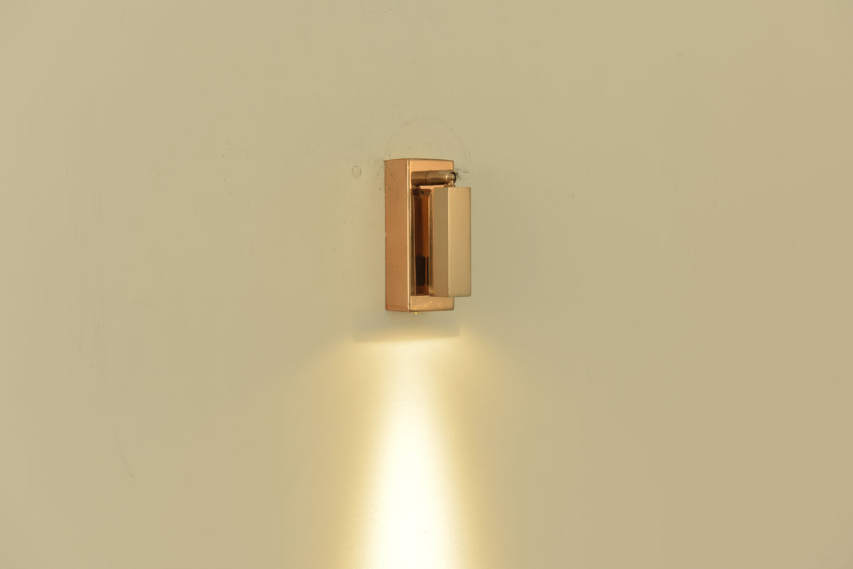 Wandlamp Vero in rosegoud ingeklapt en brandend met een lichtbundel omlaag